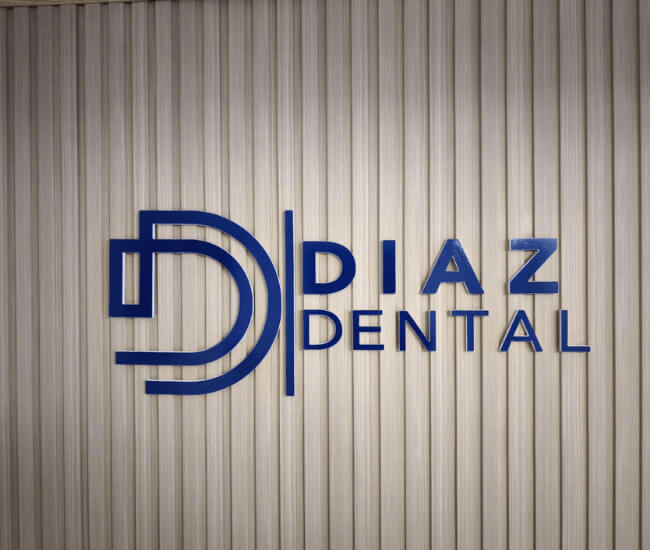 Logotipo y texto de Diaz Dental en azul sobre una pared beige a rayas verticales. El logotipo presenta dos grandes letras D superpuestas a la izquierda del nombre de la empresa, que representan una clínica dental en La Cuesta especializada en ortodoncia y tratamientos dentales.
